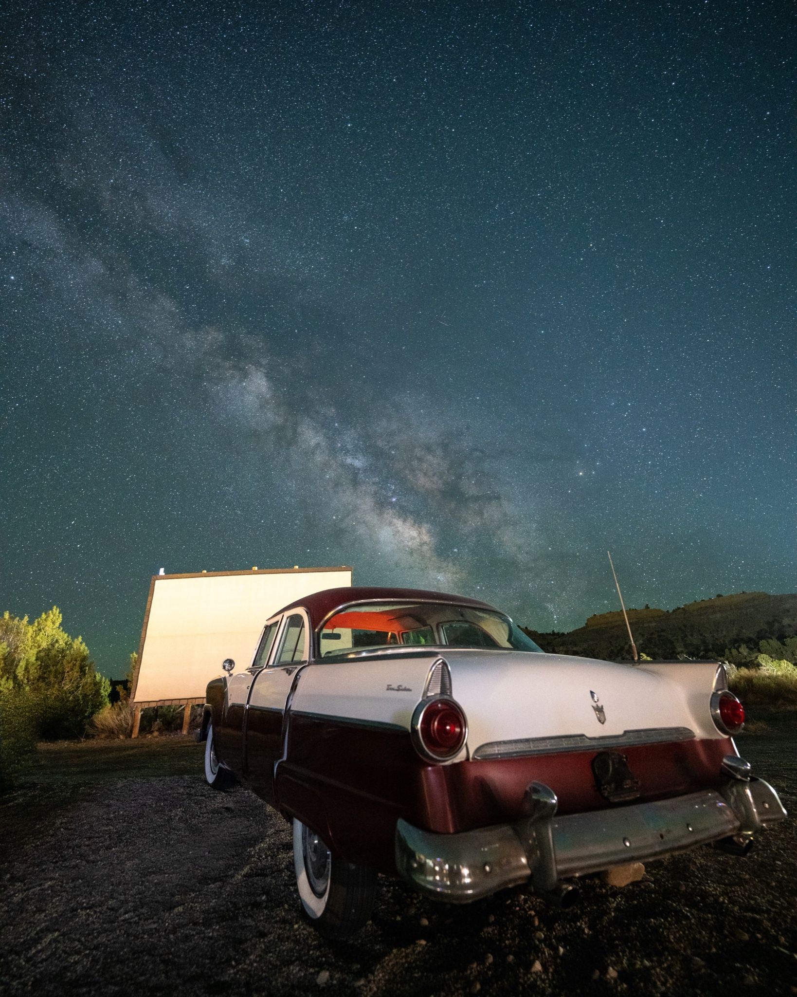 A drive-in screen still standing, a car still parked at it, and the galaxy doing the projecting.